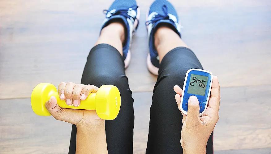 Person checking blood sugar with glucometer while holding a dumbbell