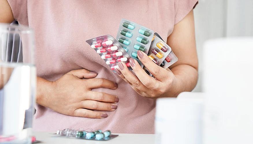 woman with antibiotic-associated diarrhea holding pills and her stomach