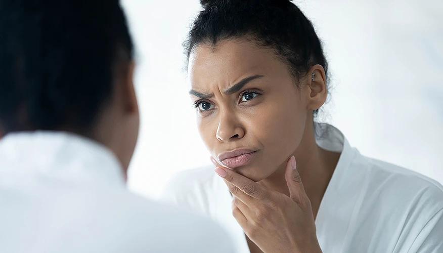 woman examining her skin in a mirror, illustrating common nighttime cleansing mistakes